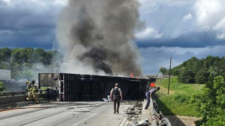 Overturned tractor-trailer sends cab into river, igniting fire and community rescue effort