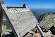 Someone carved initials into the sign at the summit of Katahdin