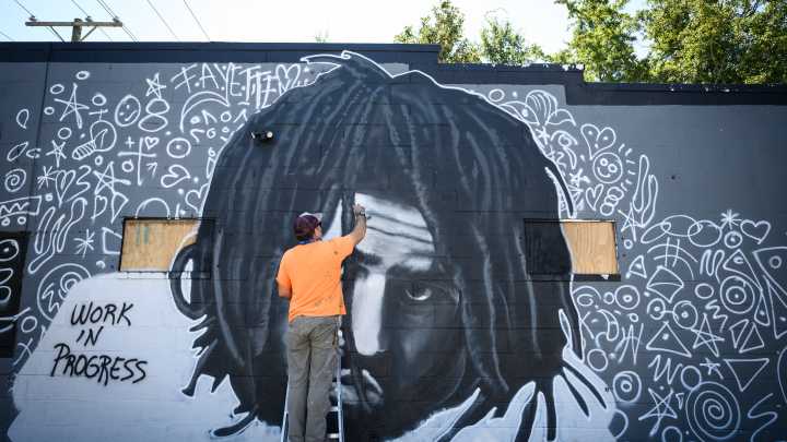 An artist works on a J. Cole mural on Murchison Road