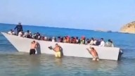 Staggering moment beachgoers push packed migrant boat BACK off Greek tourist beach after they sailed across from Libya